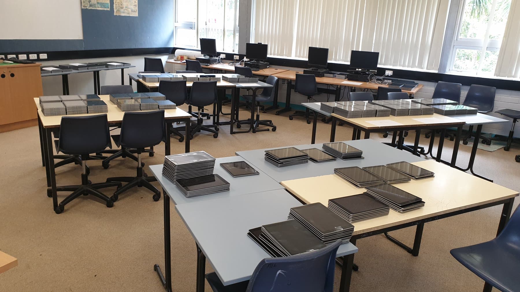 Dozens of school iPads arranged in labelled deployment stacks across classroom tables