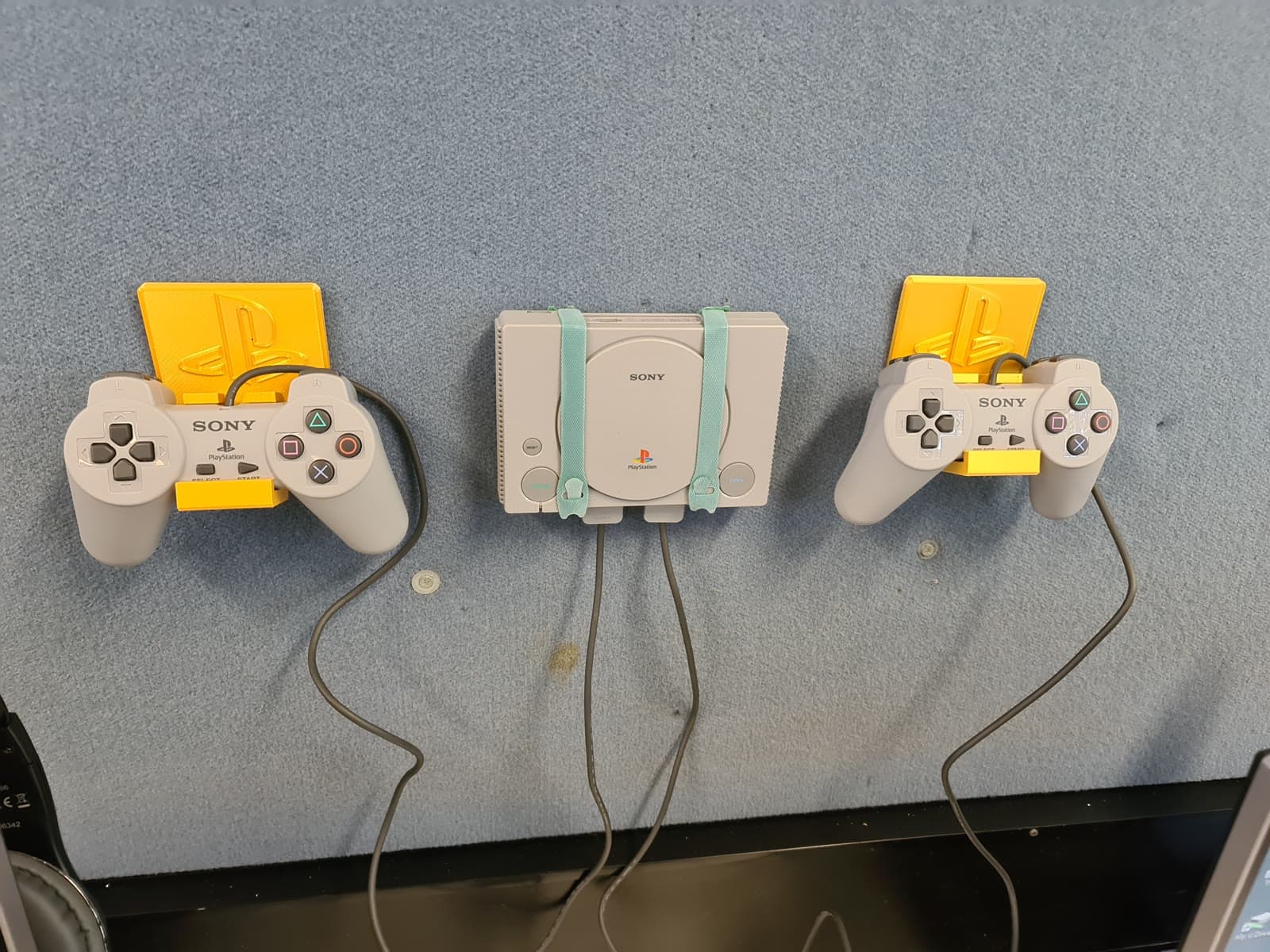 Original PlayStation hardware held safely on a wall using custom yellow 3D-printed mounts